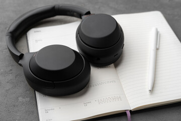 Black headphones on notepad with pen lying on gray background