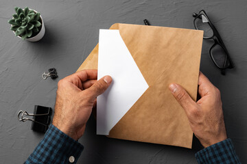 Business correspondence. Top view of man hands holding mockup envelope with letter. Copy space.