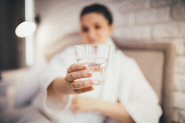 Young woman drinking clear water in the morning in her bedroom. Healthy morning rituals.