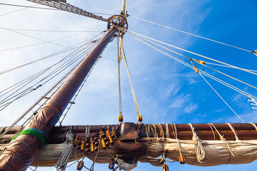 Part of an old, wooden sailing ship with a mast, folded sail and stretched sail ropes.