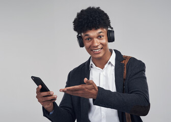 Sounds like a winning song to me. Studio shot of a young businessman using a smartphone and headphones against a grey background.