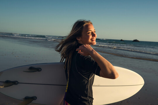 young beautiful female surfer smiling while walking towards the water in a summer day.