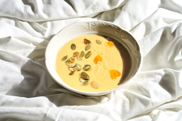 Pumpkin cream soup in a plate on a white sheet. Tough light.