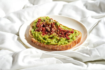 Avocado toast with sun-dried tomatoes in a plate on a white sheet. Tough light. Selective focus