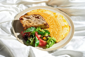 Omelet with melted cheese, vegetable salad and toast in a plate on a white sheet. Tough light.