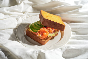 Toasted salmon and avocado sandwich in a plate on a white sheet. Tough light.