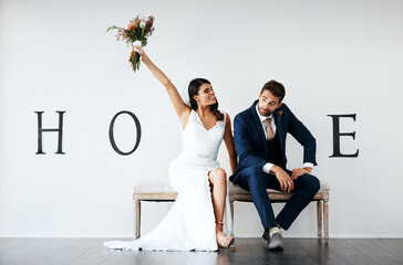 Who wants the bouquet. Concept studio shot of a bride and groom making an V in the word love against a wall.
