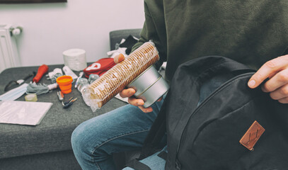 Young man packing the bag with documents, water,food, first aid kit and other items needed to survive