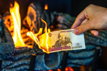 Man's hand holding a one hundred Russian rubles on fire. Currency crisis in Russia. The Russian...