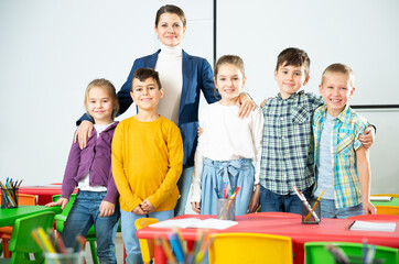 Portrait of young female teacher and happy school children posing together in classroom