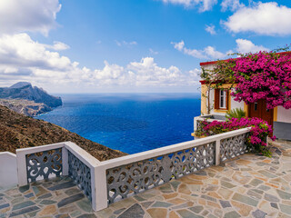  A bright violet colored bougainvillea on a house with an outstanding panoramic view of the blue sea and sky. Olympos town, Karpathos island, Greece.