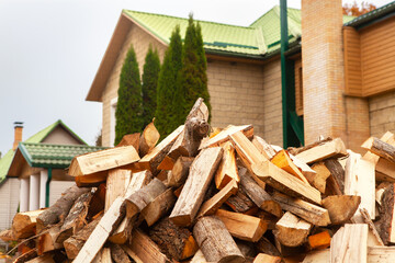 A pile of split firewood for heating the house, unloaded in the yard, against the backdrop of the house, natural heating sources.