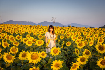 Fototapeta na wymiar Asian pretty woman smiling and standing beside a large sunflower field
