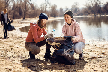 Smiling eco-friendly volunteers picking up garbage together on beach.