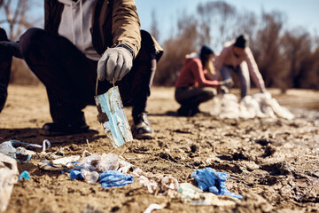 Close-up of environmentalist picking up medical face mask while cleaning trash in nature.