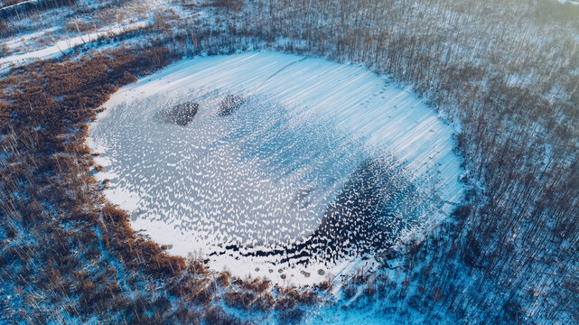 Frozen round winter lake ice aerial view. Beautiful clear blue ice stock photo from bird's eye view. Selective focus, blurred background.