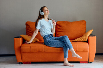 Obraz premium pretty woman listening to music with headphones on the orange sofa technologies