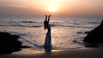 Woman dancing on the shore of the beach. Exotic woman looking at sunset at the horizon dancing...