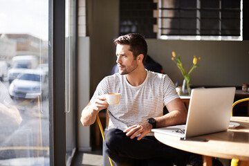 Waiting for inspiration. Shot of a young man working on a laptop in a cafe and drinking coffee.