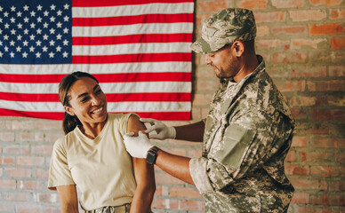 Young medic applying a band aid to a soldier's arm after vaccination