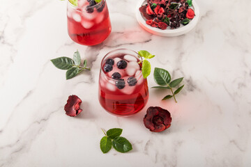 tonic vitamin drink from rose petals hibiscus with blueberries, mint leaves, ice cubes in glasses on a marble table. iced tea. © Marina