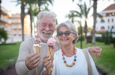 Close-up on two melting ice cream cones, held in the hand by a cheerful senior couple. Elderly...