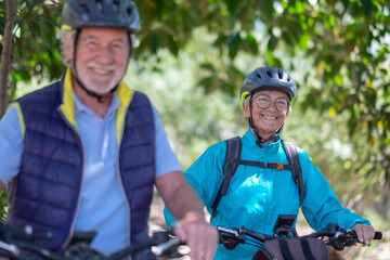 Active caucasian senior couple with electrobikes standing outdoors in the park. Two happy elderly people running in nature enjoying healthy lifestyle