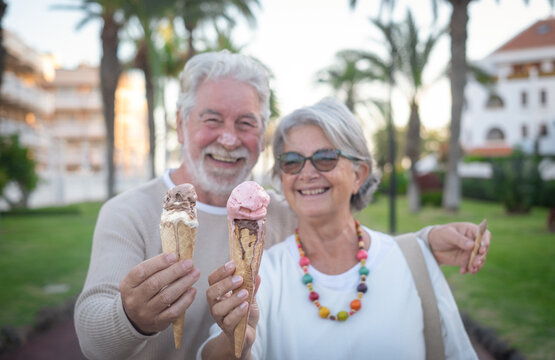 Close-up on two melting ice cream cones, held in the hand by a cheerful senior couple. Elderly people smiling looking each other in the eyes enjoying vacation or retirement