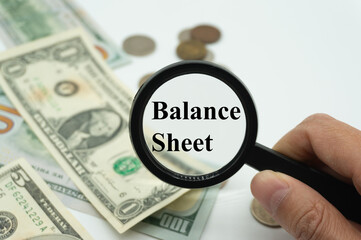 Magnifying glass showing the words "Balance Sheet".Background of banknotes and coins.basic concepts of finance.Business theme.Financial terms.