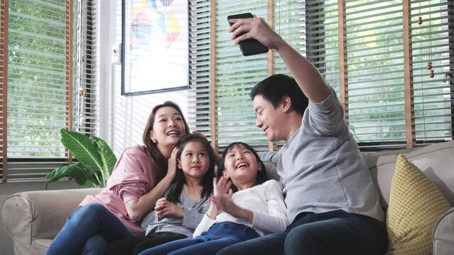 Authentic close up of asian family take photo selfie with smartphone in living room at home. Father, mother and children enjoyment with photography while being quarantine at home. Happy family at home