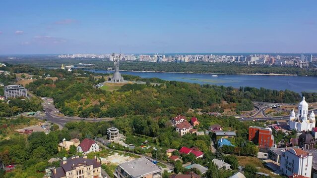 Capital of Ukraine - Kyiv city. Top view of cityscape, blue Dnipro, traffic on bridge over river and beautiful huge green trees in foreground. Real time full hd video footage.