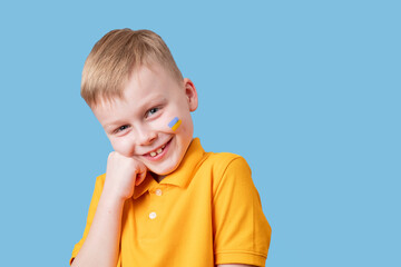 Portrait of a Ukrainian boy with a drawing flag on his cheek, cheerfully smiling at the camera. isolated on blue background