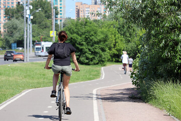 Girl in shorts riding on a bicycle on a path in a green city park. Woman cyclist, spring or summer...