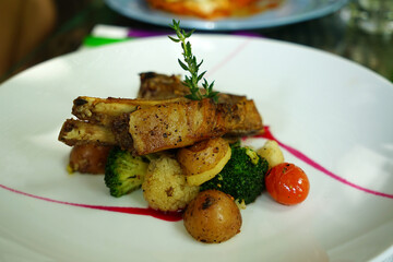 Spicy hot grilled spare ribs from a summer BBQ served with hot chili pepper and fresh tomatoes on an old vintage wooden cutting board

