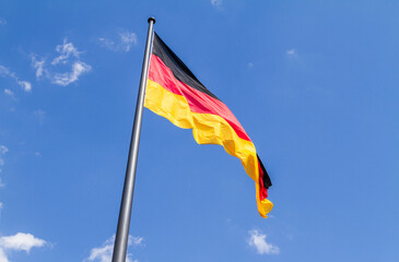 National Flag of Germany fluttering on a pole, against blue sky.