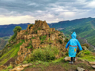 A boy on the background of Gamsutl village in the Caucasus mountains, on top of a cliff. Dagestan Russia June 2021