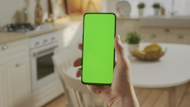 Handheld Camera: Point of View of Young Man at Home Sitting on Kitchen Room With Green Mock-up Screen Smartphone. Boy is Watcing Content Without Touching Gadget Screen. Modent Technology