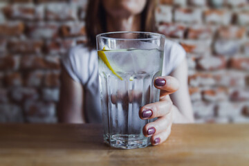 Attractive young girl drinking water in a pub. Woman having glass of fresh water with lemon.