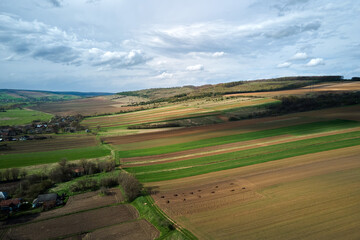 Aerial view of plowed agricultural fields with cultivated fertile soil prepared for planting crops between green woods in spring