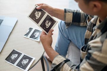 Young father holding ultrasound photo of newborn baby, maternity and family concept