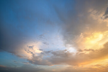 Dramatic cloudy sunset landscape with puffy clouds lit by orange setting sun and blue sky