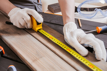 Carpenter is measuring length of wood planks or timbers by measuring tape or ruler. Carpenter workspace, craftsman entrepreneur. - obrazy, fototapety, plakaty