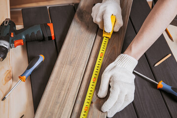 Hands in gloves of joiner in carpentry. Carpenter is measuring length of wood planks or timbers by...