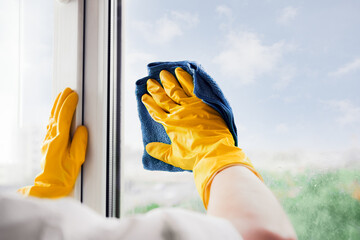 Man in yellow rubber gloves cleaning window glasse with cleaner spray detergent and squeegee...
