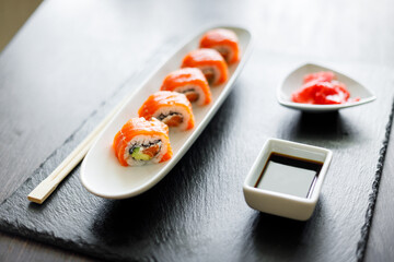 Sushi roll covered with salmon served in long plate on slate board