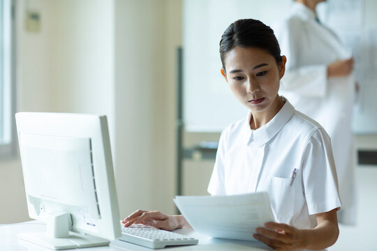 資料を見ながらPCを操作する女性看護師