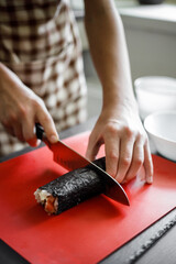 Young teeange boy cutting sushi roll at home kitchen