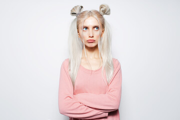 Studio portrait of offended, pretty blonde girl with two hair buns, on white.