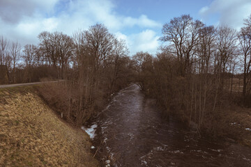rapid river in valley, bare trees, walkway on riverside	