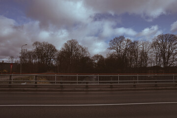 bridge railing, asphalt road, forest ahead